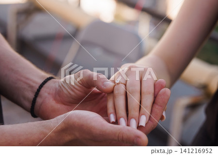 Close up of a man holding a womans hand with a diamond engagement ring in soft natural outdoor lighting. 141216952