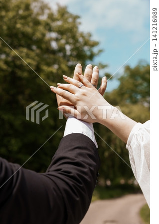 Newlywed couple holding hands showing engagement ring during outdoor wedding ceremony in green nature park. Newlywed couple holding hands showing engagement ring during outdoor wedding ceremony in green nature park. 141216989