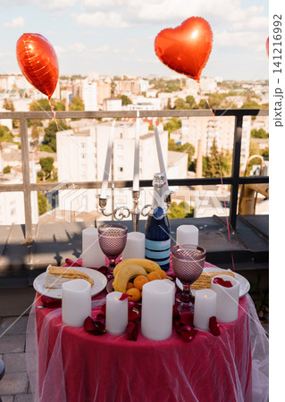 Romantic dinner table on city rooftop with red heart balloons champagne and candles at sunset Romantic dinner table on city rooftop with red heart balloons champagne and candles at sunset 141216992