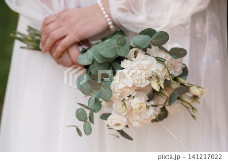 Bride holding white floral bouquet with green eucalyptus leaves in a white wedding dress Bride holding white floral bouquet with green eucalyptus leaves in a white wedding dress 141217022