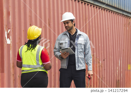 African American female and Latino male worker using tablet, checking workflow loading freight containers from Cargo freight, import export concept. African American female and Latino male worker using tablet, checking workflow loading freight containers from Cargo freight, import export concept. 141217294