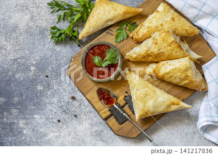 Traditional asian food. Vegetarian samsa (samosa) stuffed with potato with tomato sauce on a stone surface. Healthy breakfast,  snack. Top view flat lay background. Copy space. 141217836