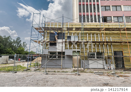 Workers are installing mineral wool insulation on the building's facade using scaffolding. The sky is clear and the construction site is active 141217914