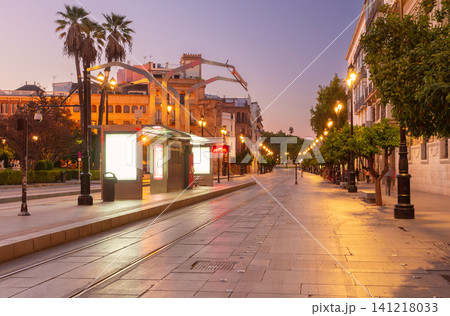 Evening view of Avenida de la Constitucion in Seville, Spain, with illuminated tram stop, historic architecture, and empty pedestrian boulevard in the city center. 141218033