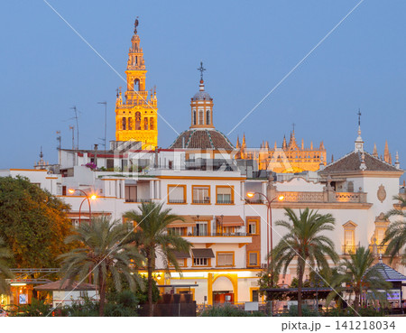 Illuminated skyline of historic Seville featuring the Giralda bell tower, cathedral rooftops, and traditional Andalusian architecture at blue hour. Illuminated skyline of historic Seville featuring the Giralda bell tower, cathedral rooftops, and traditional Andalusian architecture at blue hour. 141218034