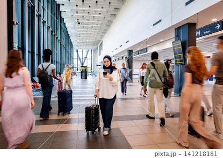 Muslim woman checking phone while traveling through busy airport Muslim woman checking phone while traveling through busy airport 141218181