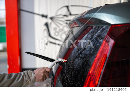 Person cleaning and wiping back window of a vehicle with water squeegee tool at manual car wash. Person cleaning and wiping back window of a vehicle with water squeegee tool at manual car wash. 141218405