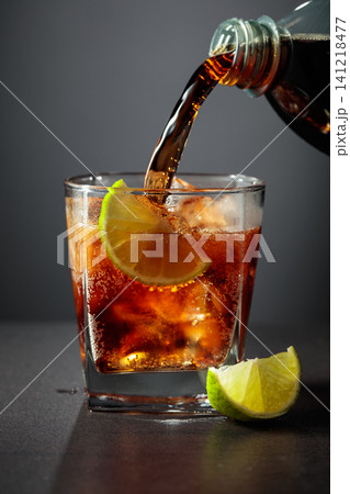 Refreshing cocktail with lime, cola and ice in a glass on a black table. Refreshing cocktail with lime, cola and ice in a glass on a black table. 141218477
