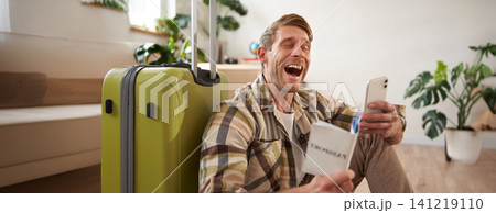 Happy man with suitcase, holding passport and using smartphone, going on holiday 141219110