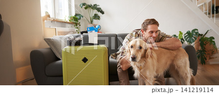 Portrait of happy young man going on holiday, travelling with his dog companion, sitting with golden retriever near suitcases and tickets Portrait of happy young man going on holiday, travelling with his dog companion, sitting with golden retriever near suitcases and tickets 141219114