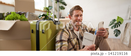 Portrait of smiling handsome tourist, man holding passport and flight tickets, sitting with suitcase Portrait of smiling handsome tourist, man holding passport and flight tickets, sitting with suitcase 141219116