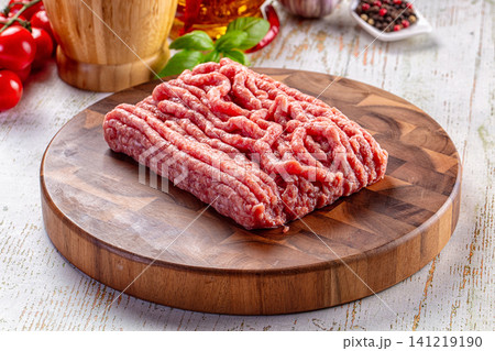 Raw ground meat on wooden cutting board with fresh ingredients Raw ground meat on wooden cutting board with fresh ingredients 141219190