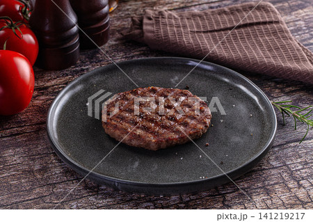 Grilled beef patty on dark plate with fresh tomatoes and rosemary on rustic wood Grilled beef patty on dark plate with fresh tomatoes and rosemary on rustic wood 141219217