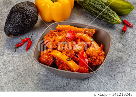 Spicy chicken curry with bell peppers in gray bowl surrounded by fresh vegetables 141219243