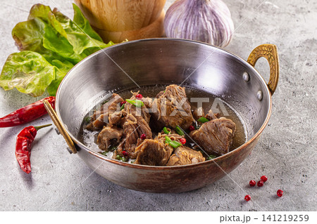 Stewed lamb in metal bowl with red chili peppers and garlic 141219259