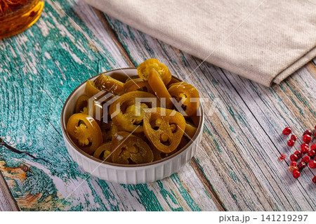 Sliced pickled jalapeno peppers in a white bowl on a rustic turquoise wooden table 141219297