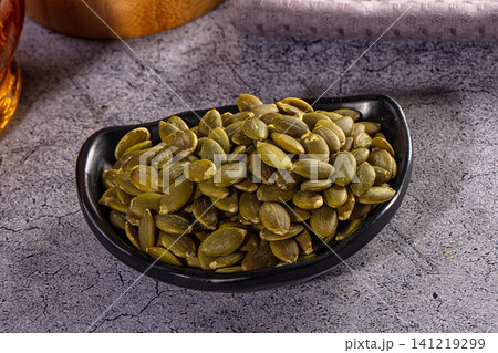 Shelled pumpkin seeds, also known as pepitas, in a black bowl on a rustic grey surface Shelled pumpkin seeds, also known as pepitas, in a black bowl on a rustic grey surface 141219299