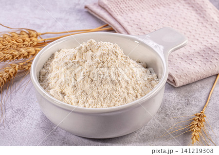 White ceramic bowl filled with fine wheat flour beside golden wheat stalks on textured surface White ceramic bowl filled with fine wheat flour beside golden wheat stalks on textured surface 141219308