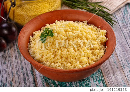 Couscous in terracotta bowl with parsley garnish on rustic wooden table 141219338
