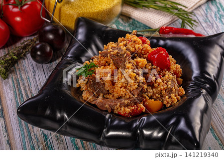 Couscous with tender beef and roasted tomatoes served in black ceramic bowl 141219340