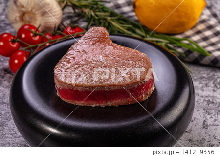 Seared tuna steak on black plate with cherry tomatoes lemon and rosemary Seared tuna steak on black plate with cherry tomatoes lemon and rosemary 141219356