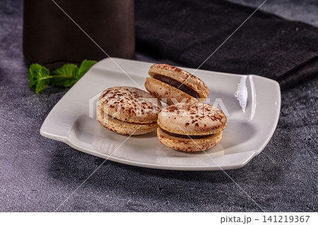 Three chocolate macarons on white plate with mint leaves Three chocolate macarons on white plate with mint leaves 141219367