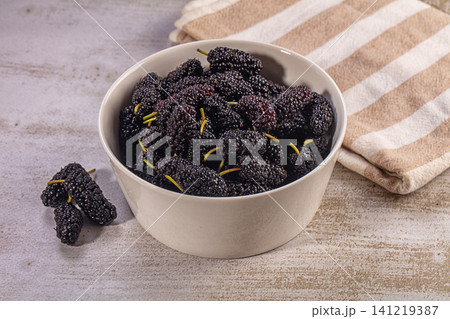 Fresh mulberries in white ceramic bowl on rustic surface with striped cloth Fresh mulberries in white ceramic bowl on rustic surface with striped cloth 141219387