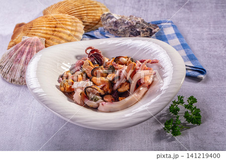Seafood salad with squid octopus mussels in white bowl surrounded by seashells and parsley 141219400