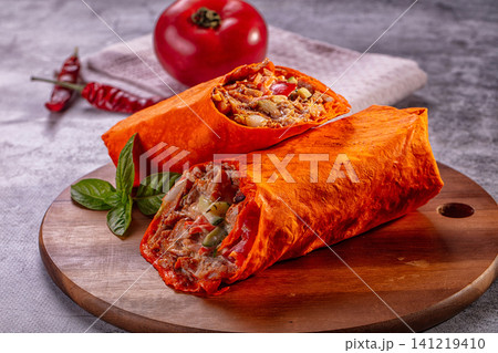 Spicy chicken shawarma wrap cut open on wooden board with tomato and chili Spicy chicken shawarma wrap cut open on wooden board with tomato and chili 141219410