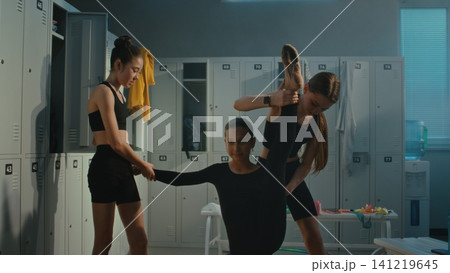 Teen Gymnasts Helping Teammate with Deep Leg Stretch in Locker Room 141219645