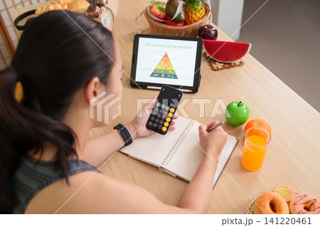 Asian woman using smartphone calculator and notebook for healthy eating meal planning Asian woman using smartphone calculator and notebook for healthy eating meal planning 141220461