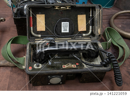 XALO, SPAIN - JUNE 20, 2026.Inside a rugged black bakelite carrying case, there is a vintage military field telephone kit. German warning labels are visible. A green canvas shoulder strap is attached  141221059
