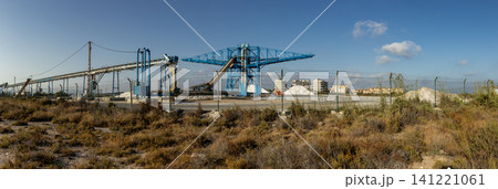 The scene shows a large industrial salt production factory in Santa Pola. Blue cranes and conveyor belts are used to process sea salt, with large piles in the background. The scene shows a large industrial salt production factory in Santa Pola. Blue cranes and conveyor belts are used to process sea salt, with large piles in the background. 141221061