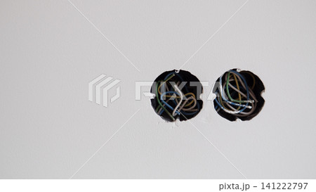 White plaster wall with two round cutouts revealing exposed electrical wires inside, showing unfinished electrical installation, rough edges, tangled colored cables, and plain White plaster wall with two round cutouts revealing exposed electrical wires inside, showing unfinished electrical installation, rough edges, tangled colored cables, and plain 141222797