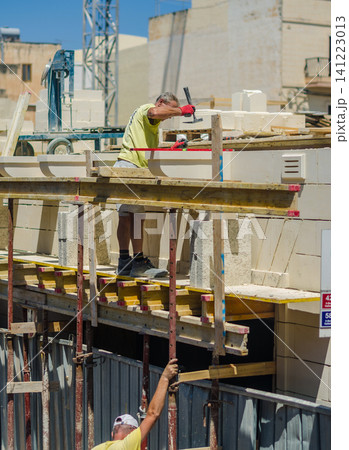 Construction worker hammering limestone building blocks on wooden scaffolding at a building site on a sunny day with second laborer. High quality photo Construction worker hammering limestone building blocks on wooden scaffolding at a building site on a sunny day with second laborer. High quality photo 141223013