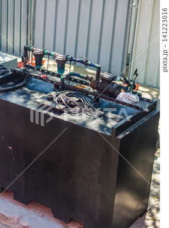 Industrial water filtration and pump system mounted on a black tank with pipes filters and electric motor at an outdoor installation. High quality photo Industrial water filtration and pump system mounted on a black tank with pipes filters and electric motor at an outdoor installation. High quality photo 141223016