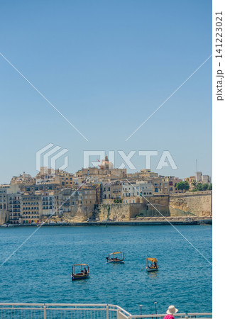 Traditional Maltese dghajsa boats crossing the Grand Harbour with historic limestone fortified town skyline in Malta on a clear summer day. High quality photo Traditional Maltese dghajsa boats crossing the Grand Harbour with historic limestone fortified town skyline in Malta on a clear summer day. High quality photo 141223021