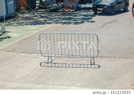 Galvanized metal crowd control barrier standing on a cracked concrete street casting a shadow with parked car in the background outdoors. High quality photo Galvanized metal crowd control barrier standing on a cracked concrete street casting a shadow with parked car in the background outdoors. High quality photo 141223035