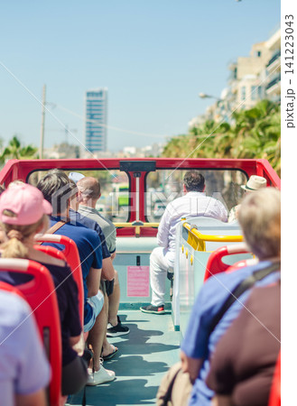 Tourists riding on the open top deck of a red sightseeing bus enjoying a city tour past palm trees and buildings on a sunny summer day. High quality photo Tourists riding on the open top deck of a red sightseeing bus enjoying a city tour past palm trees and buildings on a sunny summer day. High quality photo 141223043
