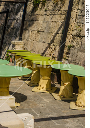Empty green round cafe tables outdoors against old stone wall, vintage bamboo style outdoor restaurant terrace in sunlight Malta. High quality photo Empty green round cafe tables outdoors against old stone wall, vintage bamboo style outdoor restaurant terrace in sunlight Malta. High quality photo 141223045