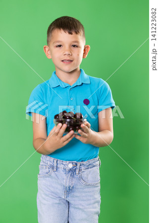 Boy in blue clothes happily eats ripe cherries on green background Boy in blue clothes happily eats ripe cherries on green background 141223082