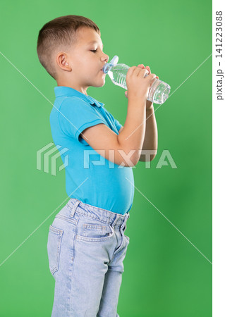 Boy in jeans with bottle of water quenches thirst Boy in jeans with bottle of water quenches thirst 141223088