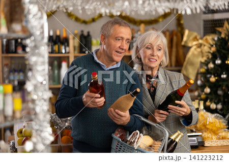 Mature husband and wife choosing wine and whiskey for Christmas celebration at supermarket Mature husband and wife choosing wine and whiskey for Christmas celebration at supermarket 141223212