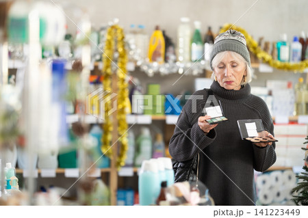 Elderly woman chooses cosmetics and eye shadow in supermarket before Christmas Elderly woman chooses cosmetics and eye shadow in supermarket before Christmas 141223449