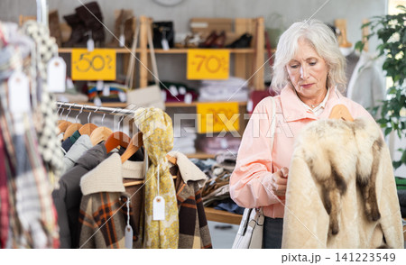 Mature woman customer examine and choose fur coat in store 141223549