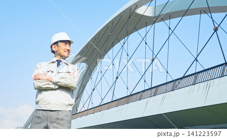 橋の前で遠くを眺める男性作業員。建設、工事、インフラ、点検、検査、メンテナンス、保守、安全、修理 141223597