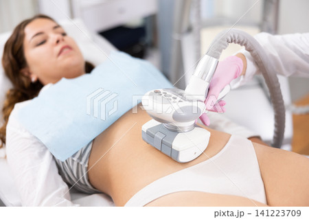 Young woman getting ultrasound cavitation body contouring treatment, anti-cellulite therapy, vacuum massage from unrecognizable cosmetologist. Hardware cosmetology for body sculpting 141223709