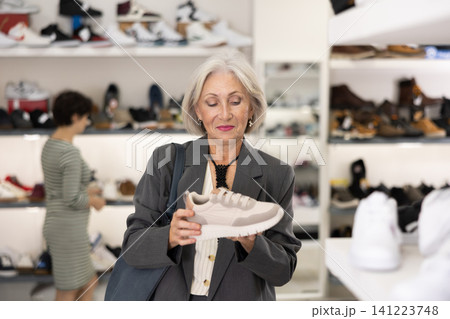 Senior woman takes samples from showcase and examines snickers Senior woman takes samples from showcase and examines snickers 141223748