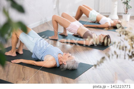 Women three generations doing different yoga exercises lying on back Women three generations doing different yoga exercises lying on back 141223771