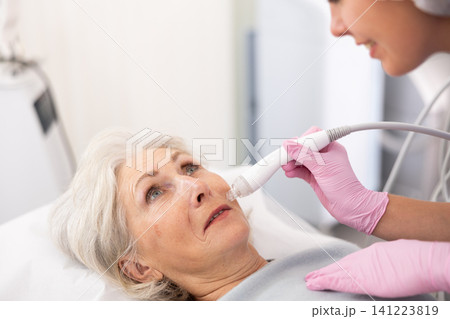 Old woman having face vacuum cleaning procedure Old woman having face vacuum cleaning procedure 141223819